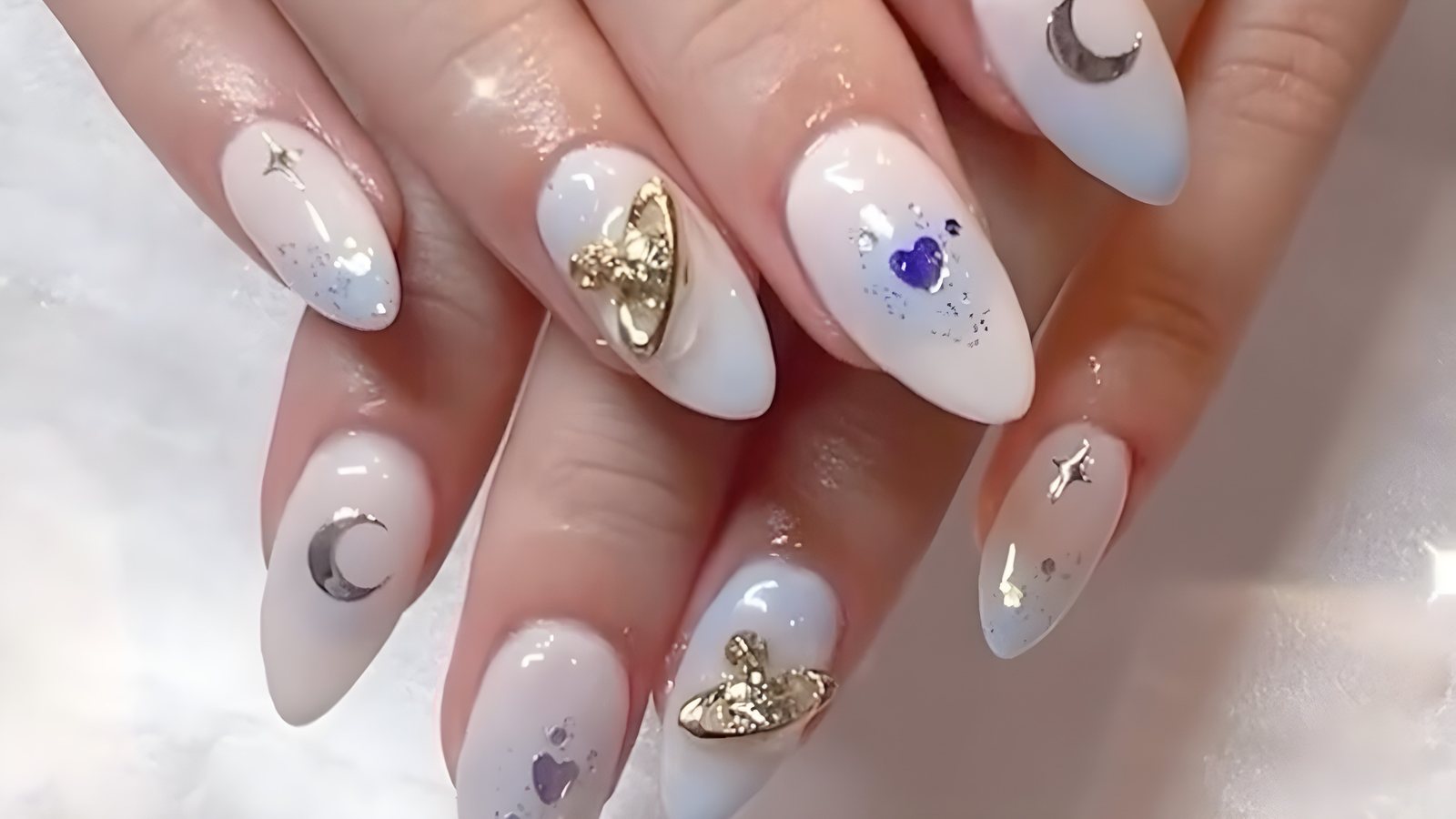 Milky white almond nails with gold charms, moons and stars