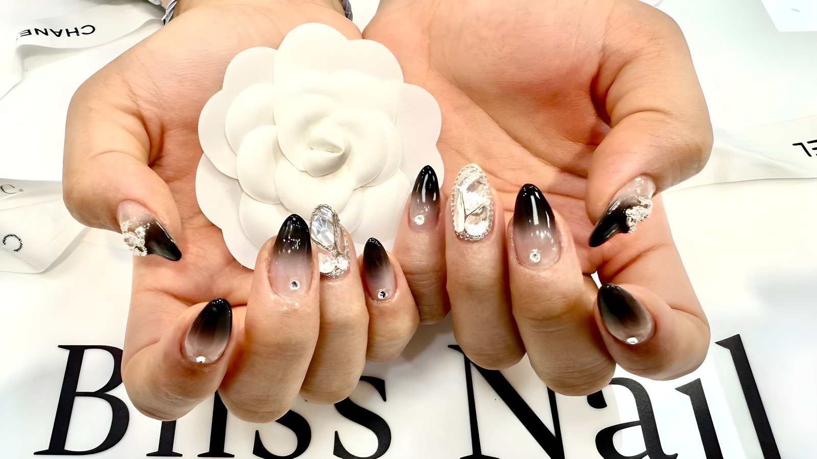 Black ombré almond nails with crystals, held around a white camellia